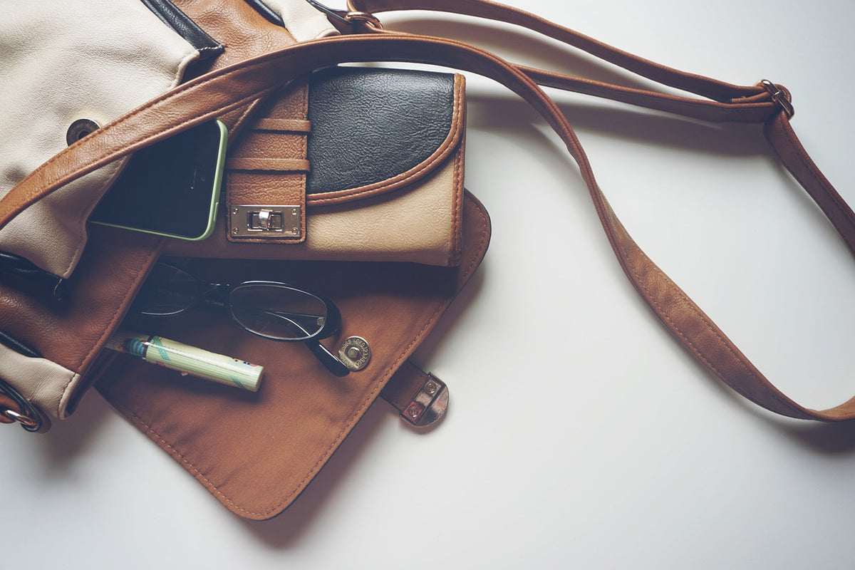 Tan leather bag opened flat with its strap and everyday contents